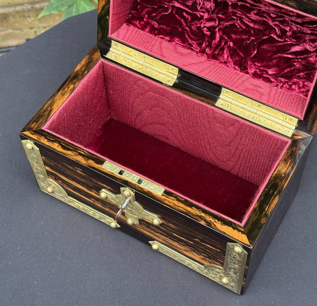 Close overhead internal view of an antique jewellery box in coromandel with engraved brass overlay.