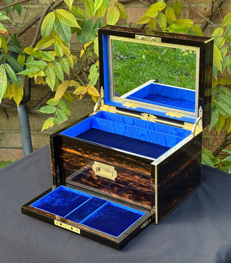 Front right internal view of an antique jewellery box in coromandel with two concealed drawers, with front flap dropped forward.