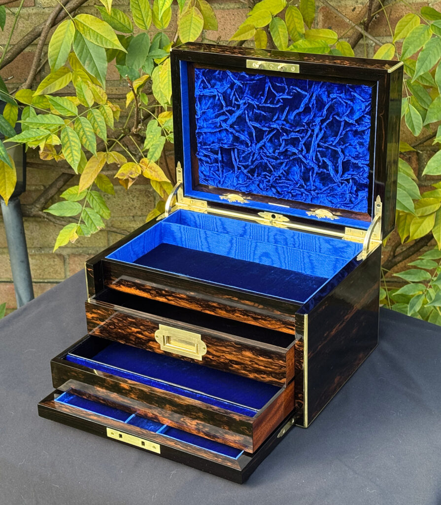 Front right internal view of an antique jewellery box in coromandel with two concealed drawers, with ruched velvet panel on display.