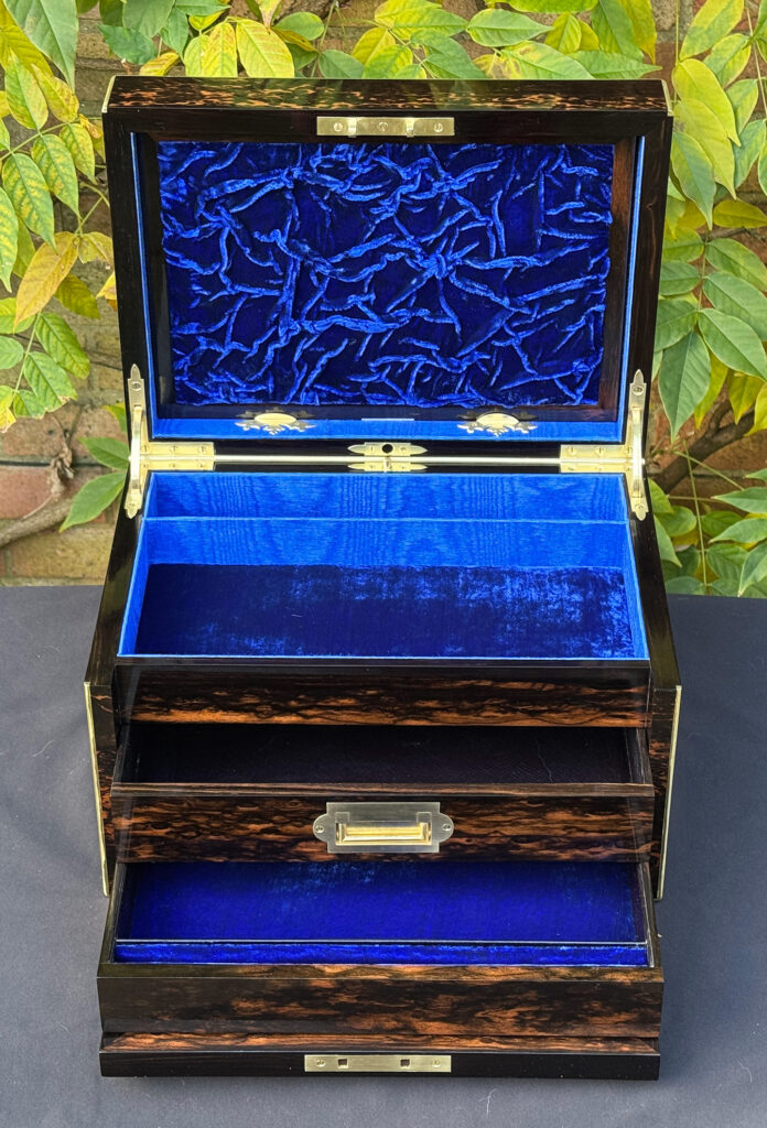 Front internal view of an antique jewellery box in coromandel with two concealed drawers, with drawers opened and ruched velvet panel on display.