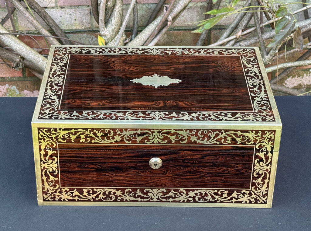 Front view of an antique jewellery box in Rosewood with scrollwork brass inlay, by Edwards.