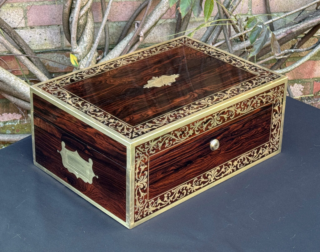Front left view of an antique jewellery box in Rosewood with scrollwork brass inlay, by Edwards.
