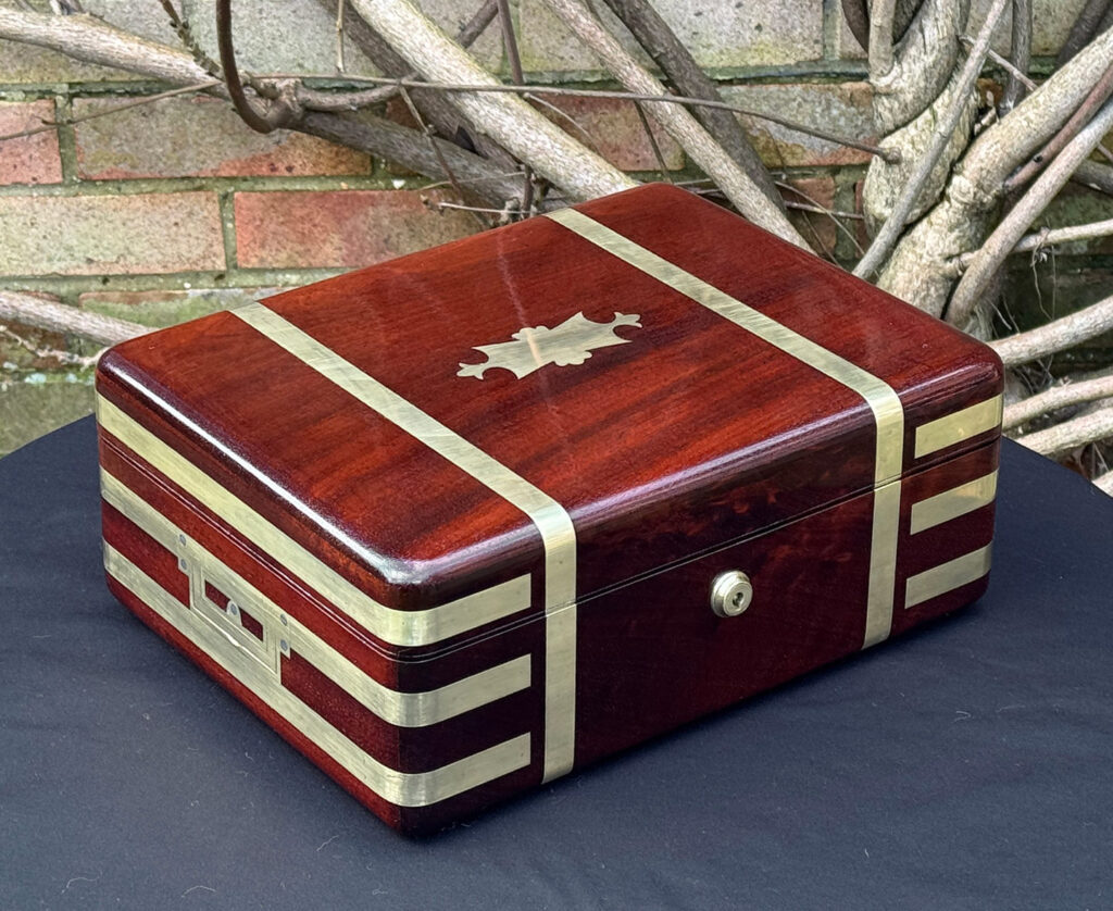 Front left view of an antique radial edged travelling jewellery box in mahogany.