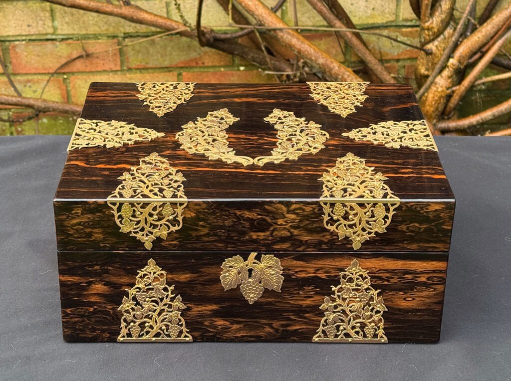 Front view of an antique sewing box in coromandel with fretwork foliate brass overlay.