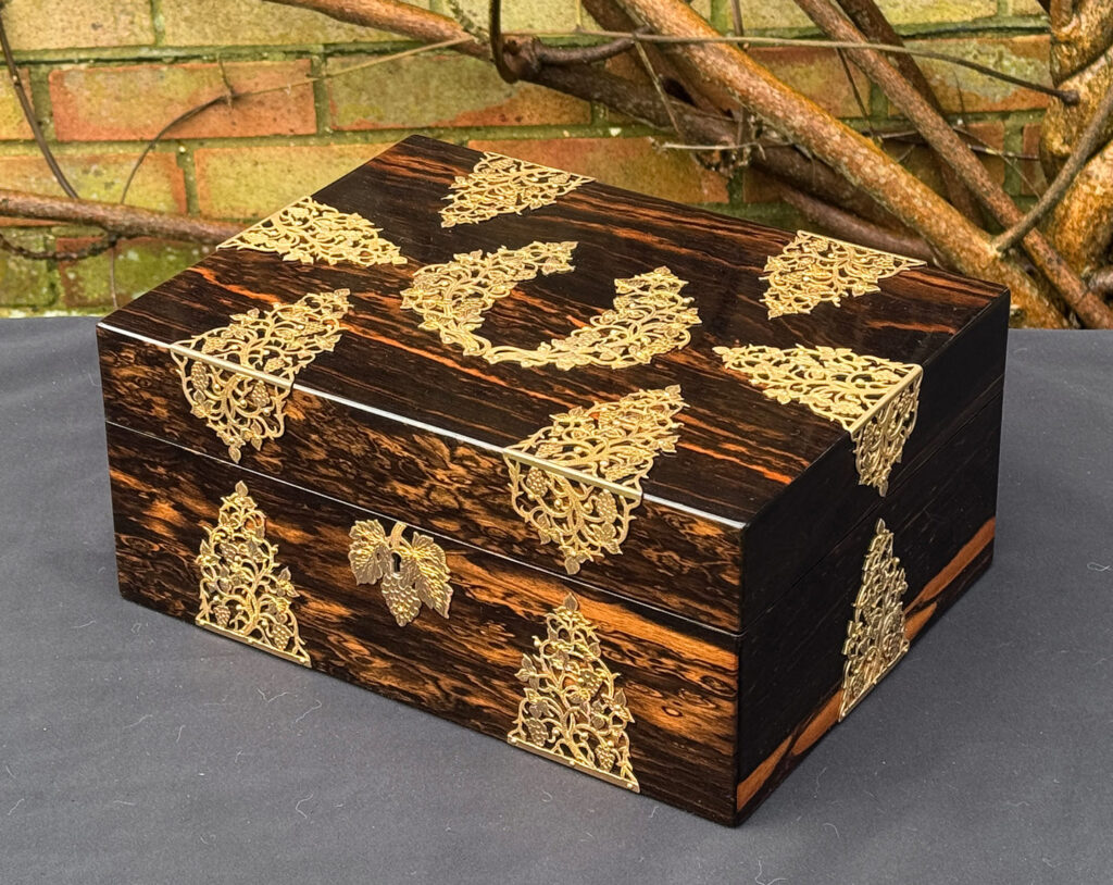 Front right view of an antique sewing box in coromandel with fretwork foliate brass overlay.
