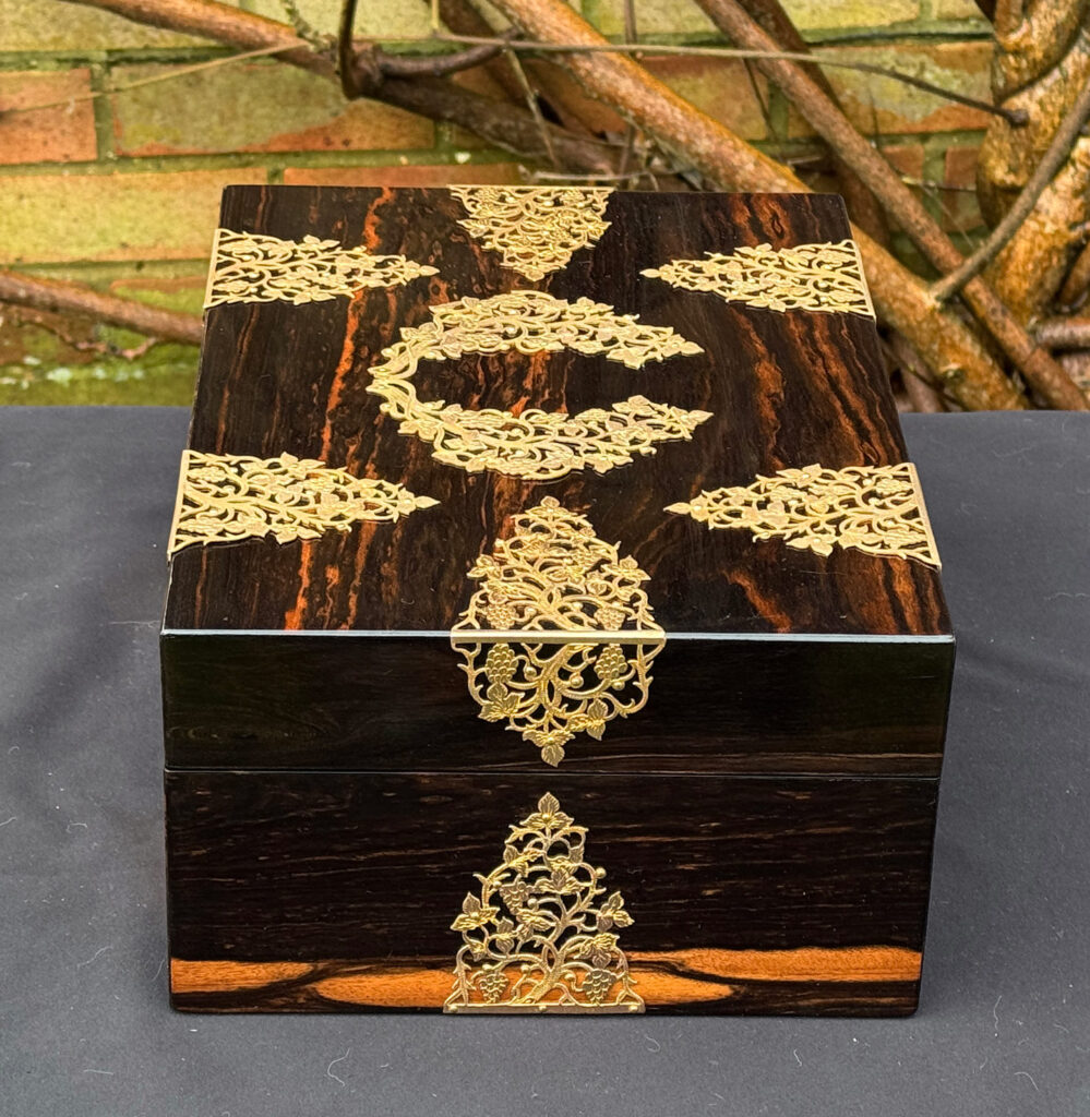 Right side view of an antique sewing box in coromandel with fretwork foliate brass overlay.