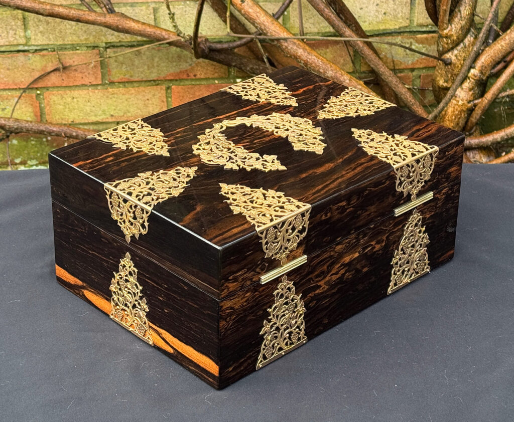 Rear right view of an antique sewing box in coromandel with fretwork foliate brass overlay.