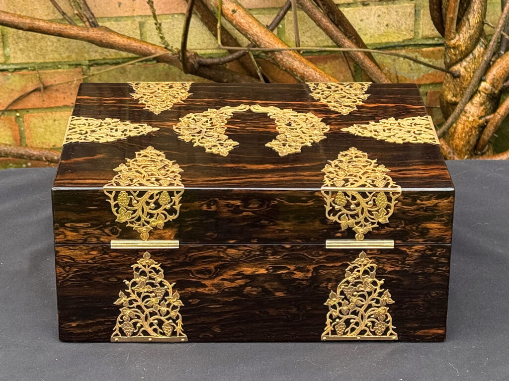 Rear view of an antique sewing box in coromandel with fretwork foliate brass overlay.