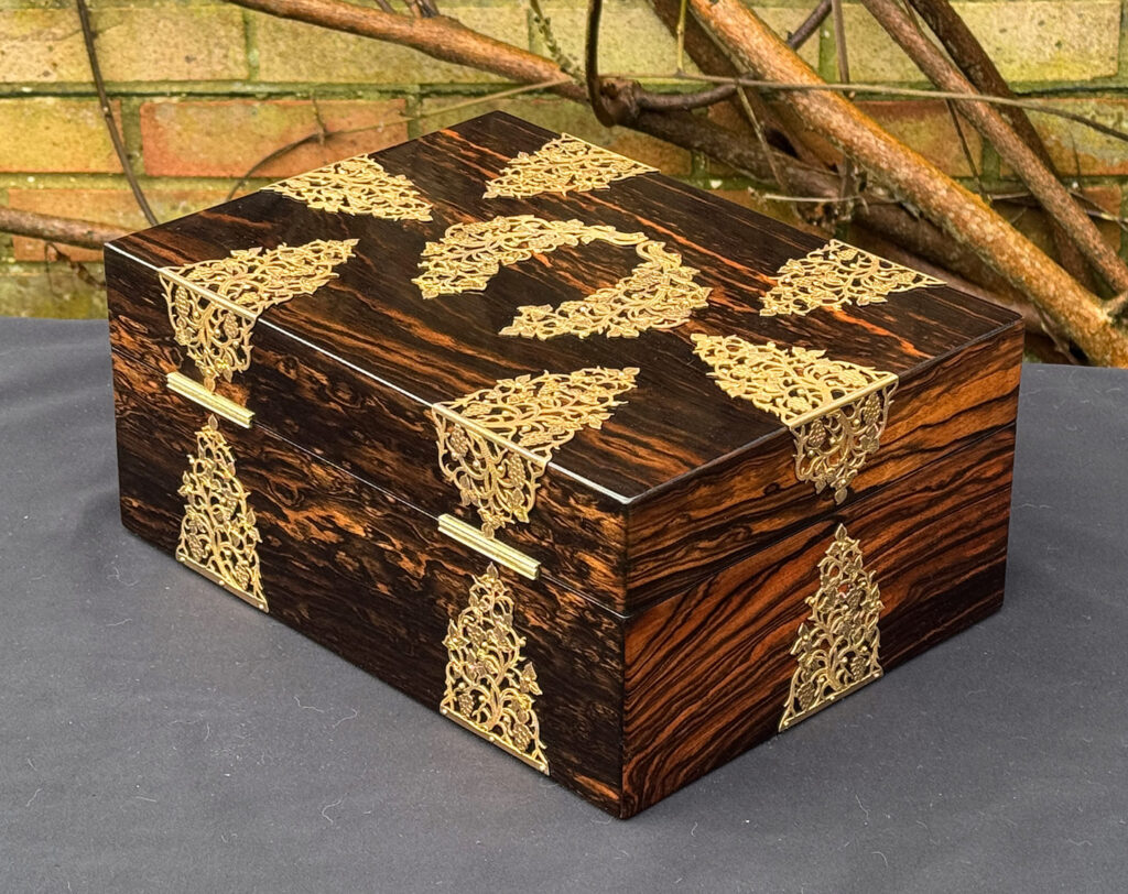 Rear left view of an antique sewing box in coromandel with fretwork foliate brass overlay.