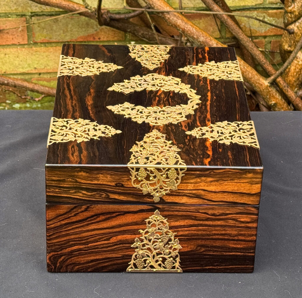 Left side view of an antique sewing box in coromandel with fretwork foliate brass overlay.