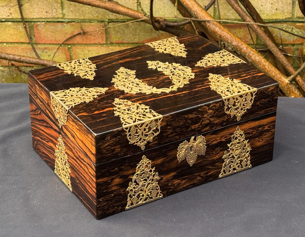 Front left view of an antique sewing box in coromandel with fretwork foliate brass overlay.