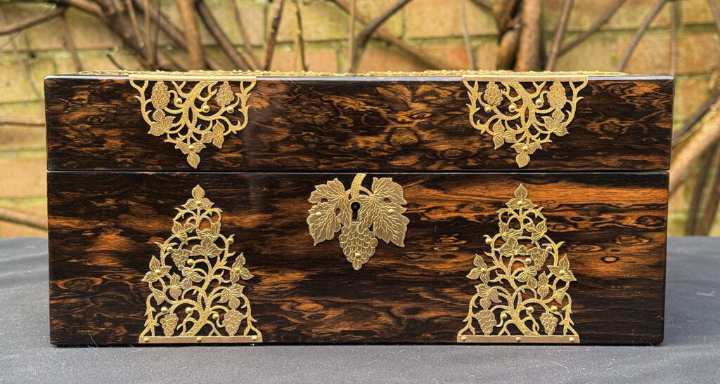 Front view of an antique sewing box in coromandel with fretwork foliate brass overlay.