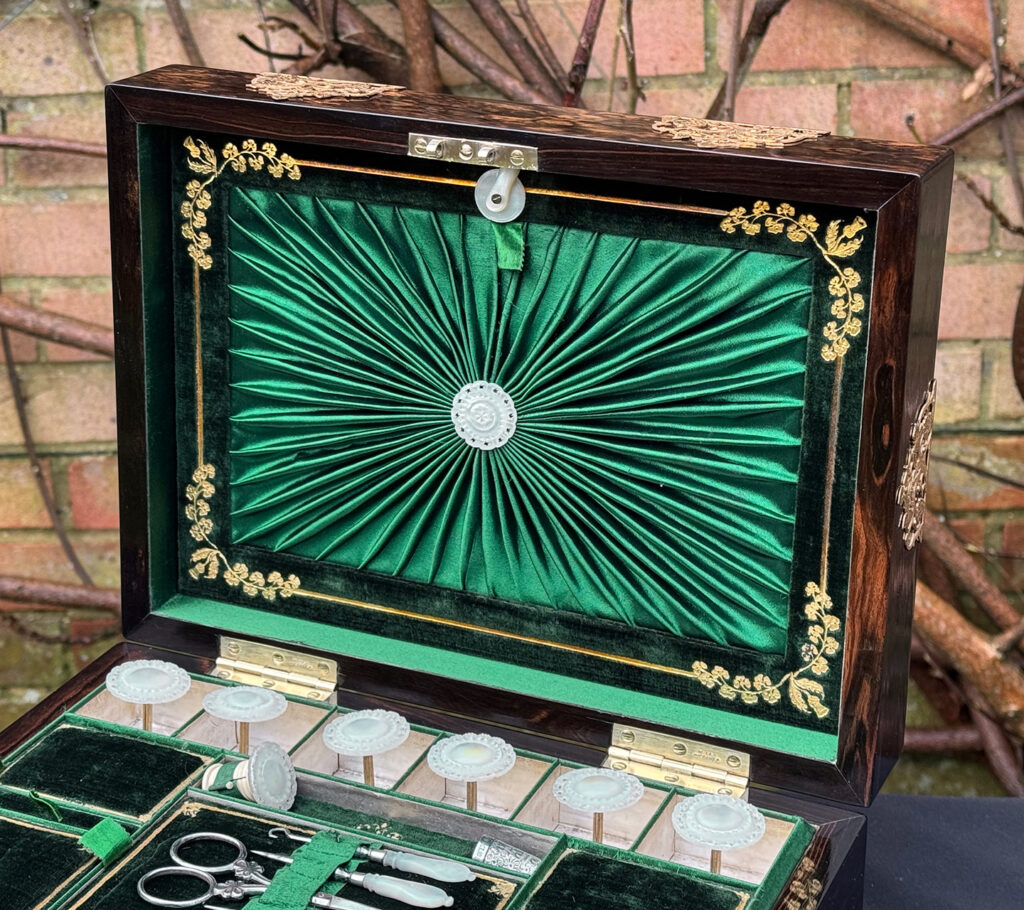 Interior view of an antique sewing box in coromandel with fretwork foliate brass overlay, focusing on the ruched silk in the lid.