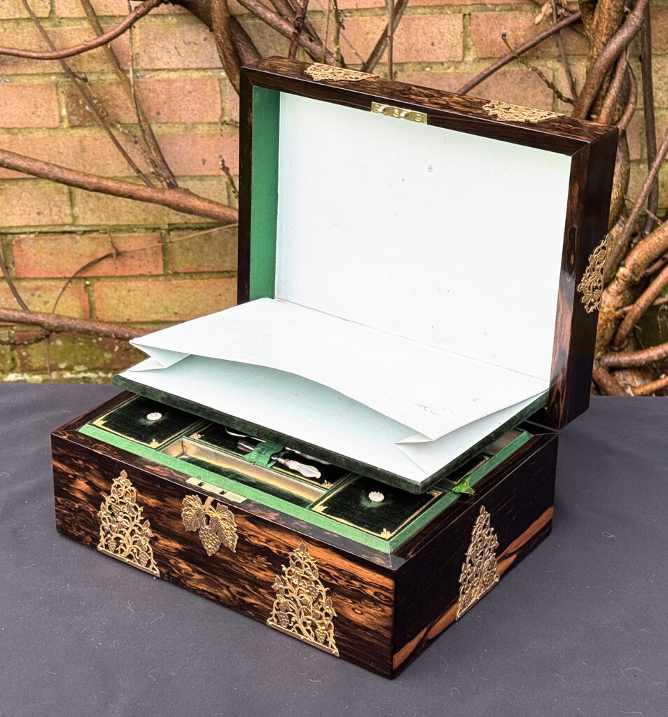 Front right interior view of an antique sewing box in coromandel with fretwork foliate brass overlay, the concealed letter wallet on view.