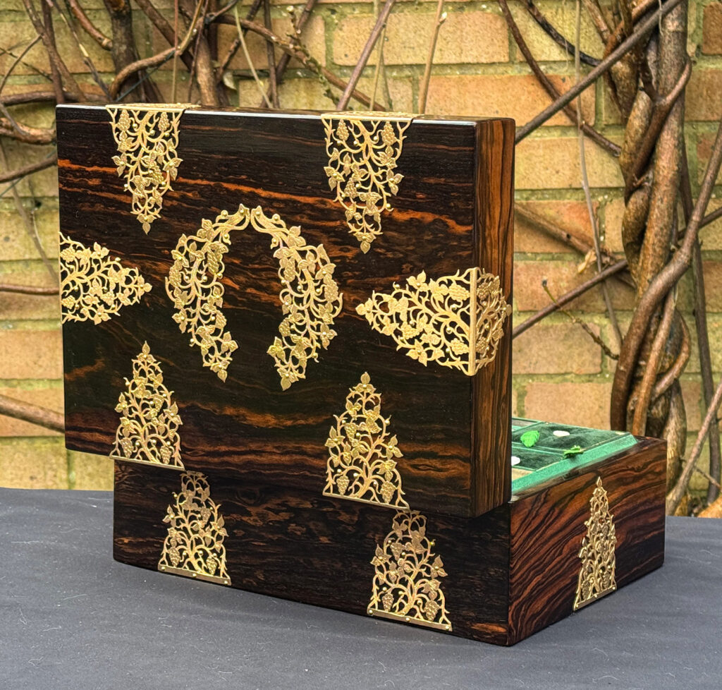 Rear opened view of an antique sewing box in coromandel with fretwork foliate brass overlay.