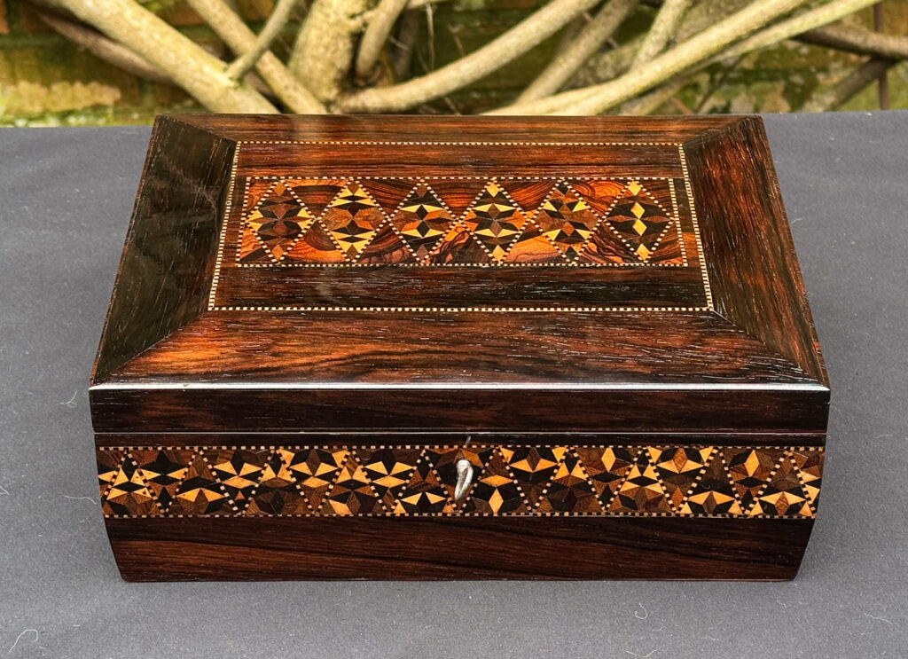 Front view of a small antique jewellery box in rosewood with parquetry inlay.