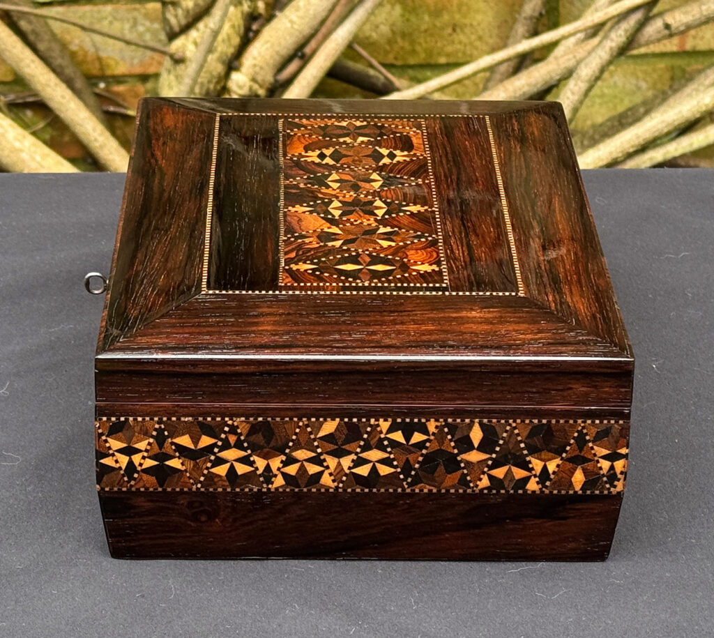 right side view of a small antique jewellery box in rosewood with parquetry inlay.