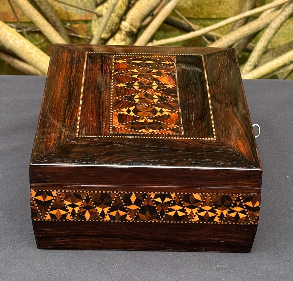 Left side view of a small antique jewellery box in rosewood with parquetry inlay.
