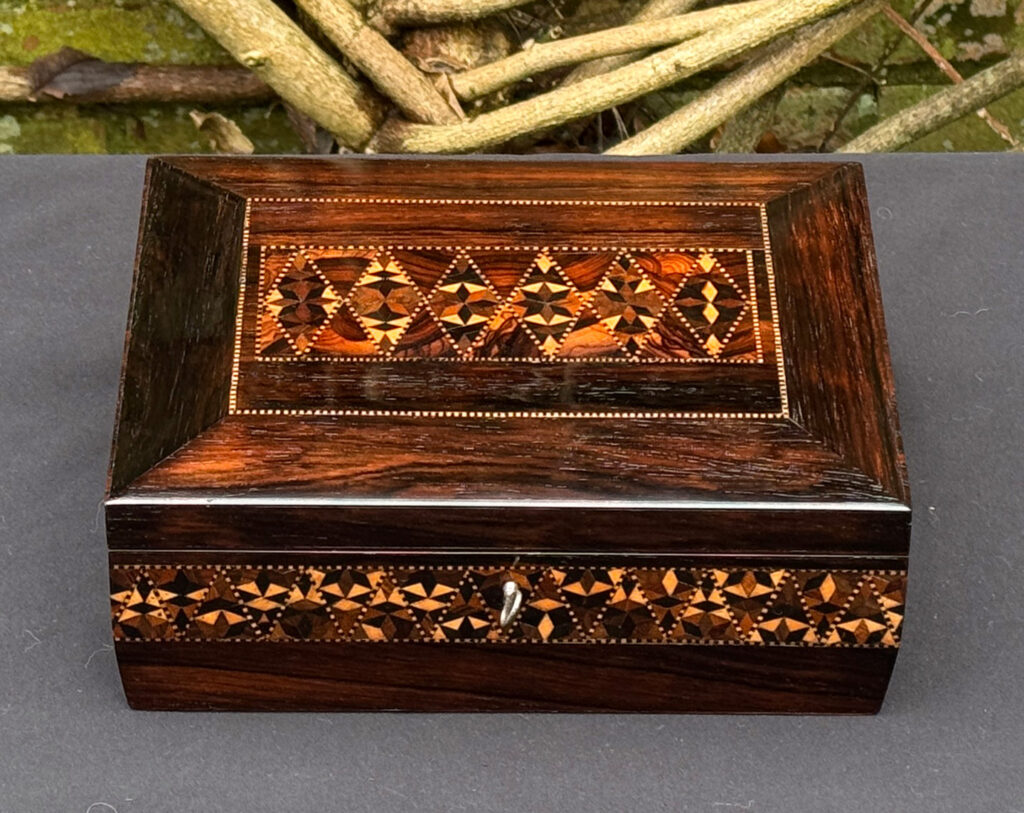 Overhead view of a small antique jewellery box in rosewood with parquetry inlay.