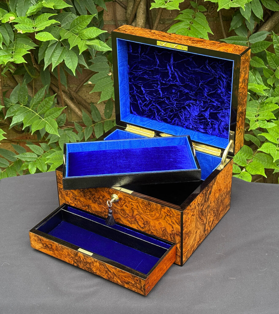 Front right interior view of an antique jewellery box in burr walnut, by George Betjemann & Sons, with lower drawer opened and tray partially removed.